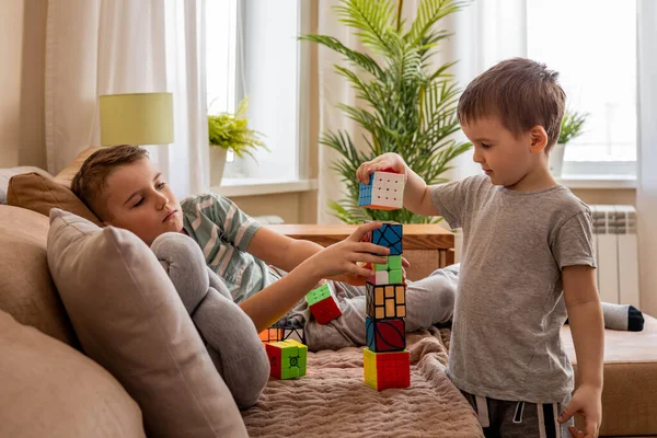 Дивні хлопчики будують вежу з різних кубиків Рубіка, граючи разом на дивані вдома. — стокове фото