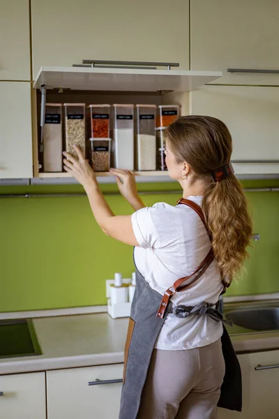 Śmiejąc się młoda kobieta gospodyni domowa pozowanie podczas ogólnego sprzątania, sprzątanie w kuchni szafy — Zdjęcie stockowe