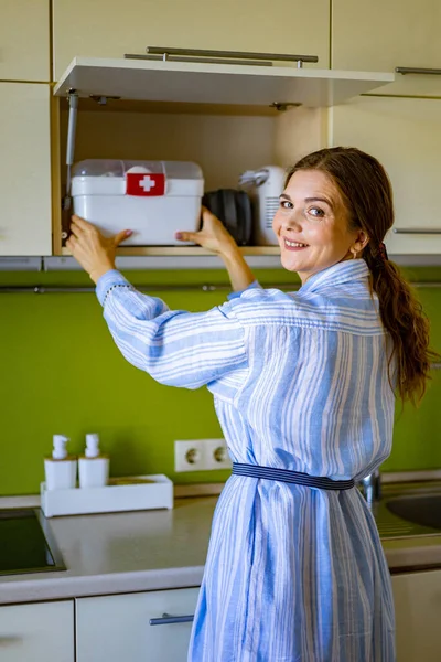 Huisvrouw zet EHBO-doos met vitaminen, medicijnen, antibiotica en genezing in keukenkast — Stockfoto