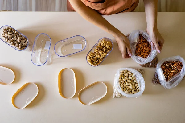 Крупный план домохозяйка руки положить орехи пластиковый пакет в контейнер коробку на деревянный стол на кухне — стоковое фото