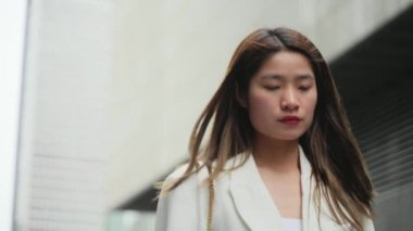 Beyaz takım elbiseli, kendine güvenen Asyalı iş kadını ofis binalarında dolanıyor iddialı kadın yavaş çekim klipsi