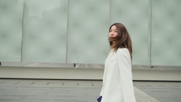 サイドビュー自信に満ちたアジアのビジネスマン女性身に着けていますホワイトスーツ歩行で都市部で深刻な野心的な女性スローモーションクリップ — ストック動画