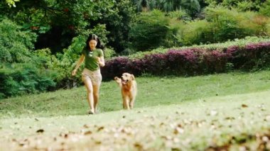 Güneşli yaz parkında genç bir bayanla birlikte köpeğiyle parkta koşan güzel Golden Retriever 'ın bulanık ağır çekimleri.