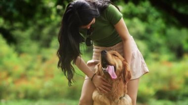 Uzun saçlı genç Asyalı kadın parkta av köpeğine dokunuyor yaz günü sevimli köpeğini kucaklayan seksi bacaklı genç Çinli kız köpekle konuşuyor.
