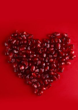 Kalp şeklinde sulu yakut nar tohumları kırmızı arka planda izole, aşk kepeği, sevgililer günü konsepti