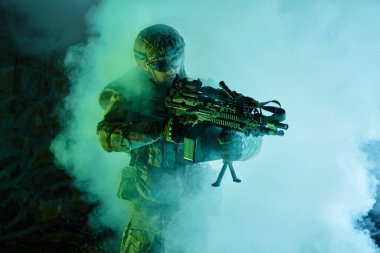 Terk edilmiş binada makineli tüfekle profesyonel ekipman içinde havalı oyuncunun portresi. Savaşta sisli ve dumanlı silahlı asker