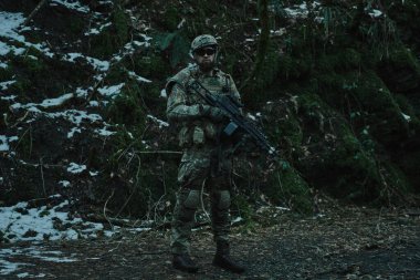 Ormanda makineli tüfekle profesyonel ekipman içinde uçan yumuşak oyuncunun portresi. Savaşta silahlı bir asker