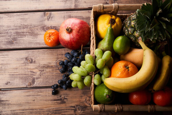 Mix of fresh juicy colorful exotic tropical fruits in basket on wooden background top view