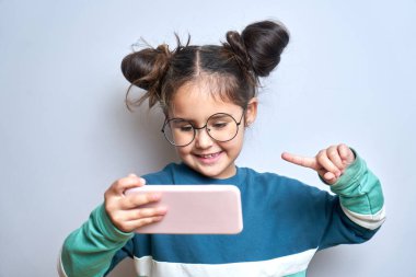 Beyaz stüdyo arka planında izole edilmiş, cep telefonu elinde, elinde akıllı telefon tutan, gülümseyen bir çocuk.