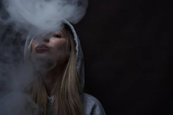 肖像画の美しいですブロンドの女の子でグレーパーカー煙蒸気煙の雲 黒のスタジオの背景に隔離されたVape — ストック写真