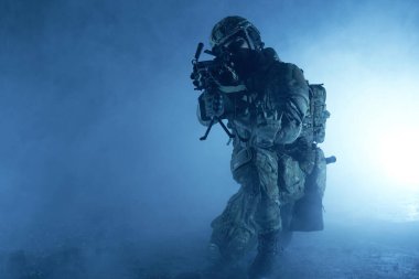 Terk edilmiş binada makineli tüfekle profesyonel ekipman içinde havalı oyuncunun portresi. Savaşta sisli ve dumanlı silahlı asker