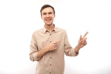 Üstü açık tişörtlü, beyaz saçlı yakışıklı esmer adam beyaz arka planda izole edilmiş ve fotokopi alanı olan boş bir yeri işaret ediyor. Ürünü gösteriyor, heyecan verici bir şey gösteriyor.