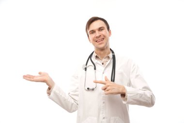 Steteskoplu beyaz önlüklü yakışıklı doktor beyaz arka planda izole edilmiş boş bir alanı işaret ediyor. Ürünü gösteriyor, heyecan verici bir şey gösteriyor.