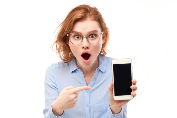 Shocked Joyful Redhead Girl Points Finger Smartphone Blank Screen Glasses — Stock Photo, Image