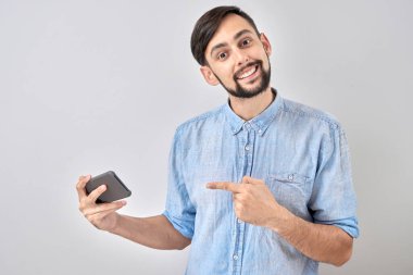 Gülen adam beyaz stüdyo arka planında izole edilmiş boş ekran cep telefonunu işaret ediyor.