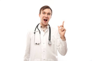 Steteskoplu beyaz önlüklü yakışıklı doktor beyaz arka planda izole edilmiş boş bir alanı işaret ediyor. Ürünü gösteriyor, heyecan verici bir şey gösteriyor.