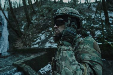 Ormanda makineli tüfekle profesyonel ekipman içinde uçan yumuşak oyuncunun portresi. Savaşta silahlı bir asker