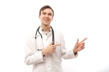Steteskoplu beyaz önlüklü yakışıklı doktor beyaz arka planda izole edilmiş boş bir alanı işaret ediyor. Ürünü gösteriyor, heyecan verici bir şey gösteriyor.