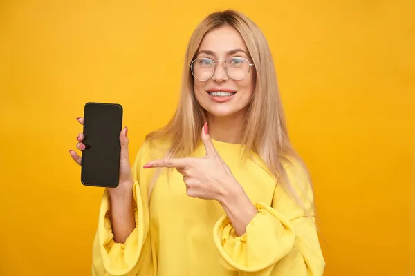 Блондинка Показывающая Экран Телефона Улыбающаяся Изолированно Желтом Студийном Фоне — стоковое фото