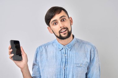 Beyaz stüdyo arka planında izole edilmiş, elinde boş cep telefonu tutan mutlu yüz şoku.