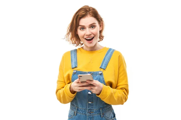 Щаслива Усміхнена Руда Дівчина Тримає Смартфон Руках Жовтому Одязі Ізольовано — стокове фото