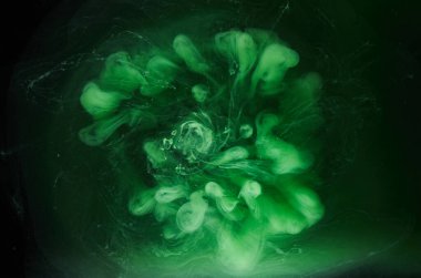 Siyah mürekkep arka planında yeşil duman, renkli sis, soyut girdaplı zümrüt okyanus denizi, su altında akrilik boya pigmenti