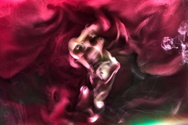 Siyah mürekkep arka planında yeşil pembe duman, renkli sis, soyut girdap dokunuşu okyanus denizi, akrilik boya pigmenti su altında