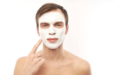 Yüzünde kozmetik maske olan yakışıklı bir adamın portresi beyaz arka planda izole edilmiş.