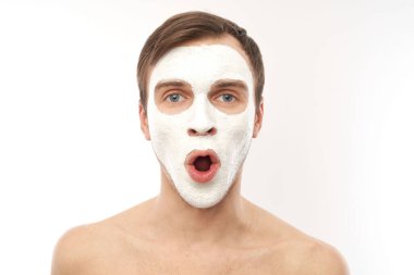 Yüzünde kozmetik maske olan yakışıklı bir adamın portresi beyaz arka planda izole edilmiş.