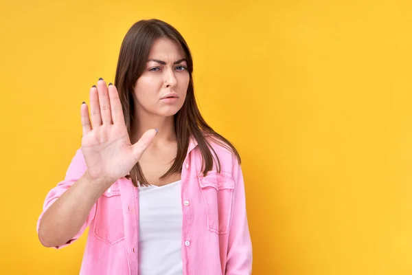 Portrait of brunette girl showing stop gesture, no please, you are refused isolated on yellow background