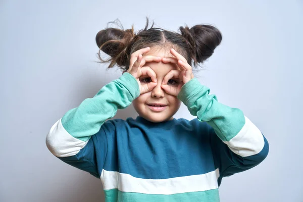 Portrait of funny brunette little girl making glasses with fingers or mask isolated on white background