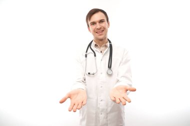 Steteskoplu beyaz ceketli yakışıklı doktor beyaz arka planda fotokopi alanı olan bir şey tutuyor. Ürünü gösterir
