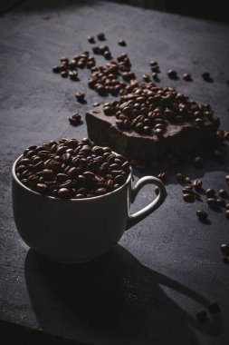 Beyaz kahve fincanı. Gri arka planda kavrulmuş kahve çekirdekleri.