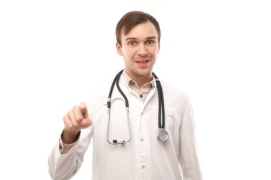 Beyaz önlüklü, arkadaş canlısı, pozitif erkek doktor portresi sizi seçiyor, beyaz arka taraftaki kamerayı işaret ediyor.