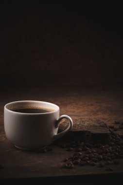 Kahverengi arka planda bir fincan taze pişmiş kahve çekirdeği.