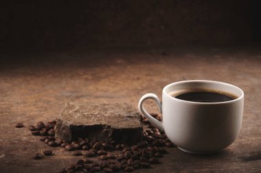 Kahverengi arka planda bir fincan taze pişmiş kahve çekirdeği.