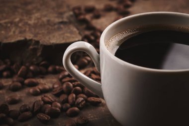 Kahverengi arka planda bir fincan taze pişmiş kahve çekirdeği.