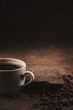 Kahverengi arka planda bir fincan taze pişmiş kahve çekirdeği.