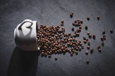 Beyaz kahve fincanı. Gri arka planda kavrulmuş kahve çekirdekleri.