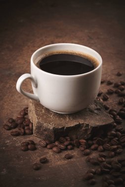 Kahverengi arka planda bir fincan taze pişmiş kahve çekirdeği.
