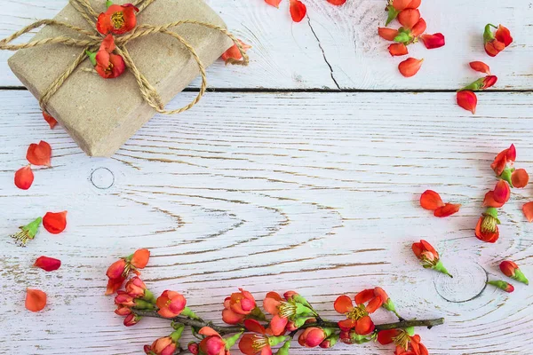 Güzel bir tatil geçmişi; kırmızı Chaenomeles japonica çerçevesi ve beyazımsı ahşap arka planda el yapımı hediye kutusu