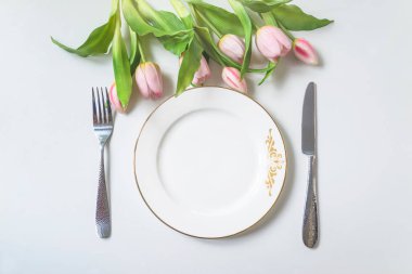 Bahar tatili mekanı, beyaz tabak, çatal ve bıçak manzarası, pembe lale demeti.
