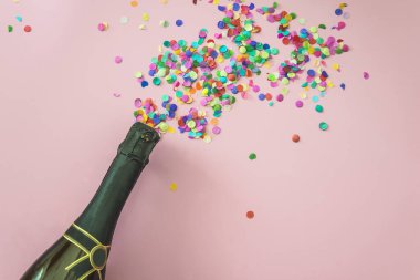 Bottle of champagne and confettis on pink background, copy space