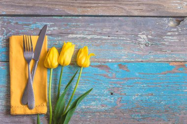 Paskalya bayramı yemeği için masa ayarı; sarı peçeteye çatal ve bıçak ve eski mavi boya ahşap arka plan