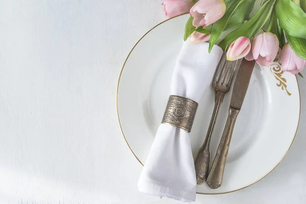 春桌布置 白色盘子顶部视图上的老式戒指中的粉红色郁金香束 复古叉子和小刀 白色餐巾 图库照片