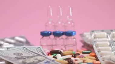 Money falls on olored drugs tablets, pills, ampoules, falling down on pink background. Pharmacy medicine and health care concept