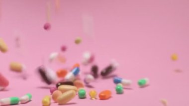 Coloured tablets and pills falling down on pink background. Pharmacy medicine and health care concept