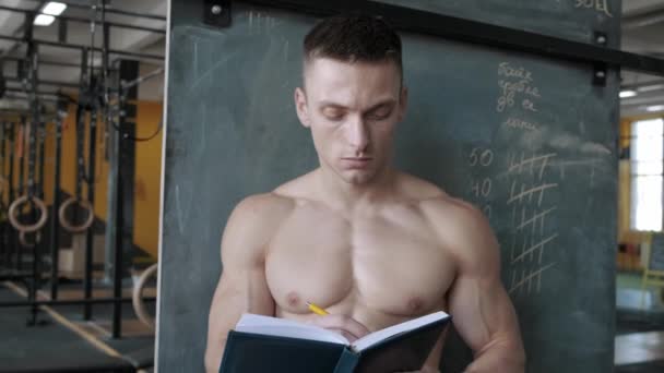 筋肉運動選手はジムでノートブックに結果を書き込みます スポーツ ウェイトリフティング ヘルスケアの概念 — ストック動画