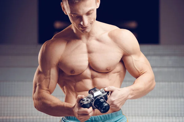 一个肌肉发达的年轻摄影师手里拿着老式相机 健身和博客概念 图库照片