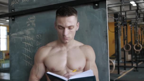 筋肉運動選手はジムでノートブックに結果を書き込みます スポーツ ウェイトリフティング ヘルスケアの概念 — ストック動画